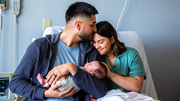 Young happy couple holding newborn baby in hospital bed